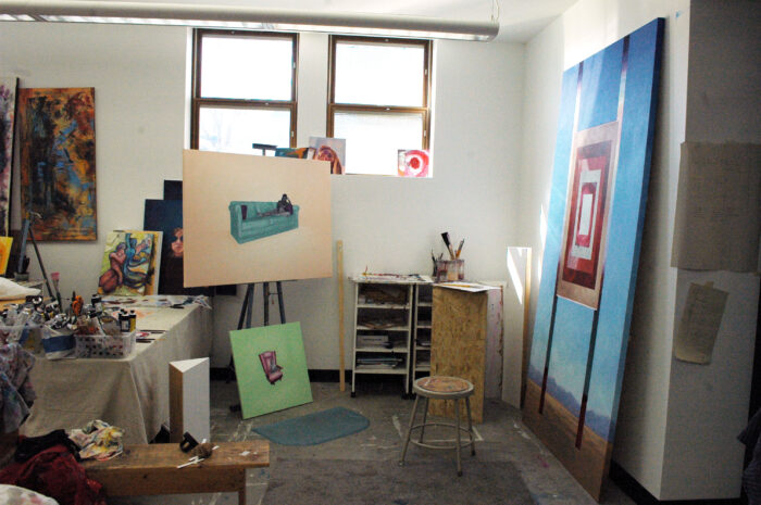 One painting sits on an easel and a larger painting leans against the wall next to it.