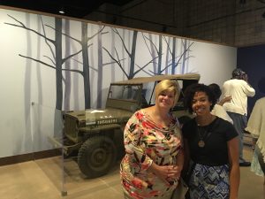 two people in the foreground, jeep in the background and in the far background there is a trees mural painted on wall