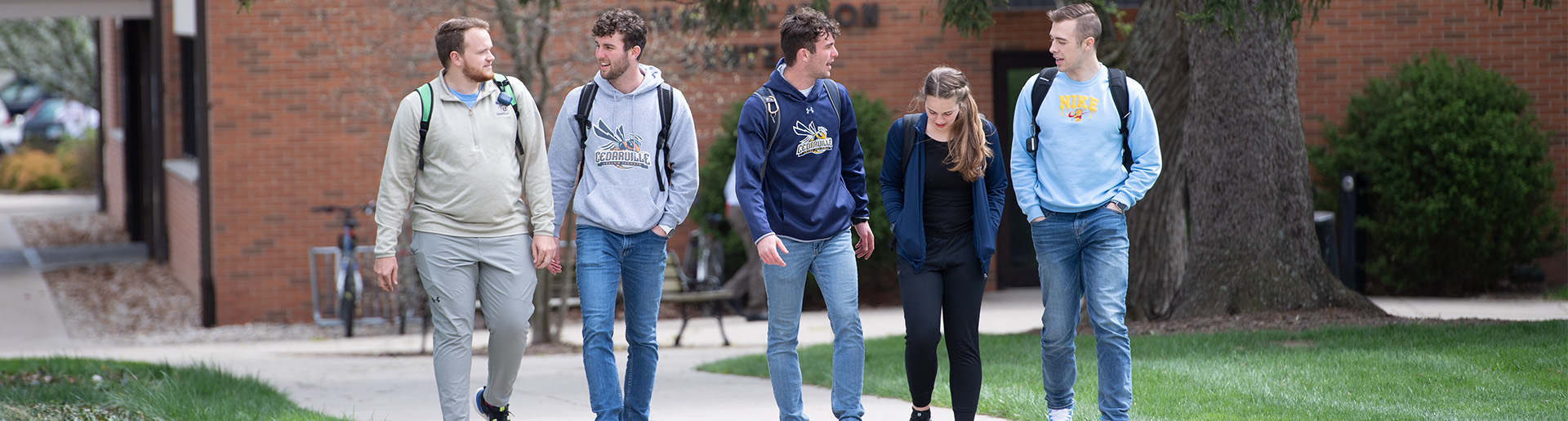 College students, four males and one female, talking together as they walk to class.